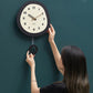 Oval wall clock being installed, dark frame and cream dial with walnut wood hands