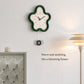 Flower-shaped wall clock with green frame and cream face, black hands; wall mounted.