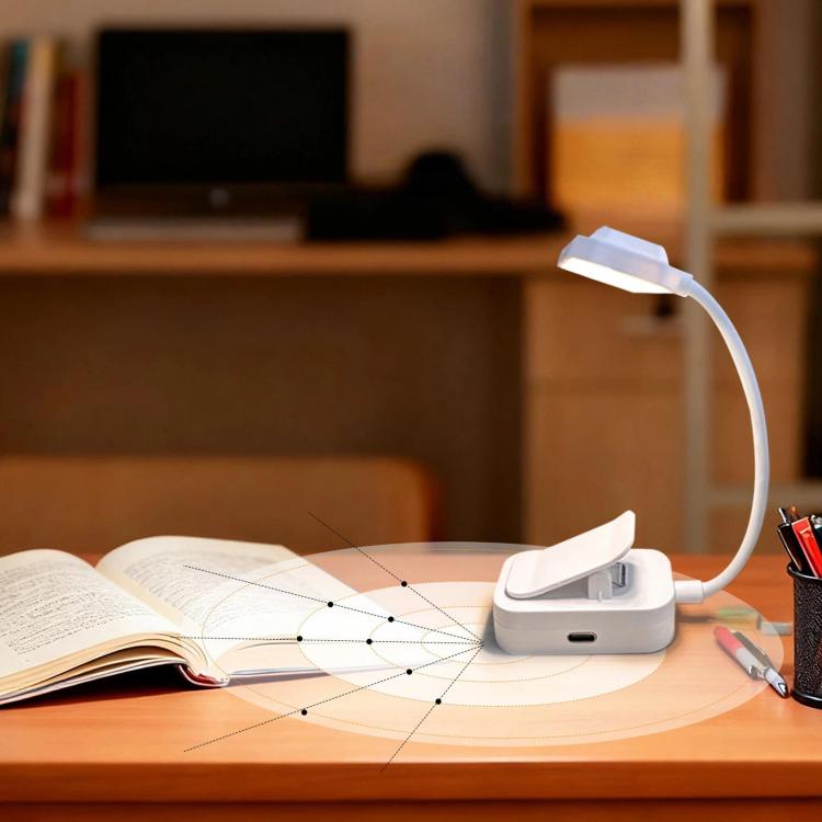 White clip-on LED lamp with glowing head over open book on study desk