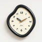 Irregular wall clock with glossy dark frame, cream dial, and gold-toned hands.