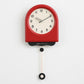 Red pendulum wall clock with cream dial and hanging pendulum weight.