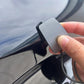 Car paint denibbing blade held by hand, silver scraper edge on car panel