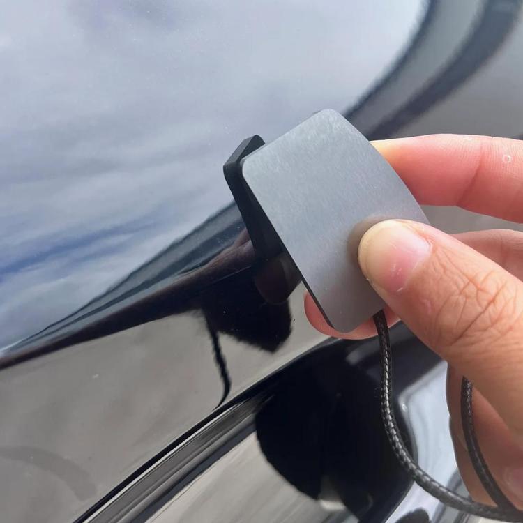 Car paint denibbing blade held by hand, silver scraper edge on car panel