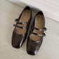 Women’s dark brown ballet flats with low cut topline, buckled straps, and perforated details