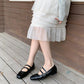 Women’s black flat ballet shoes with straps and buckles, worn with a white tiered skirt
