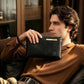 Black leather wristlet clutch bag with wrist strap and zip closure, held by a person.