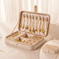 Light velvet jewelry box with hinged lid open, earring hooks, ring slots, and drawer sections