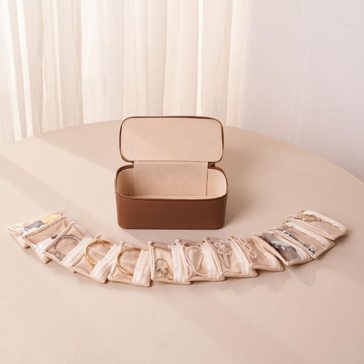 Brown PU jewelry storage case with snap-closure lid and clear zip pouches laid out