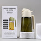 Cream white sprayer oil bottle with handle and clear glass body filled with dark oil
