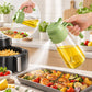 Green glass oil sprayer pouring cooking oil over food from a handle bottle