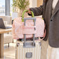 Pink nylon rolling duffel bag with green handle, zip front pocket, and wheeled base