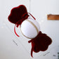 Velvet candy ornament with red scalloped ends, white oval center, gold trim and red bow