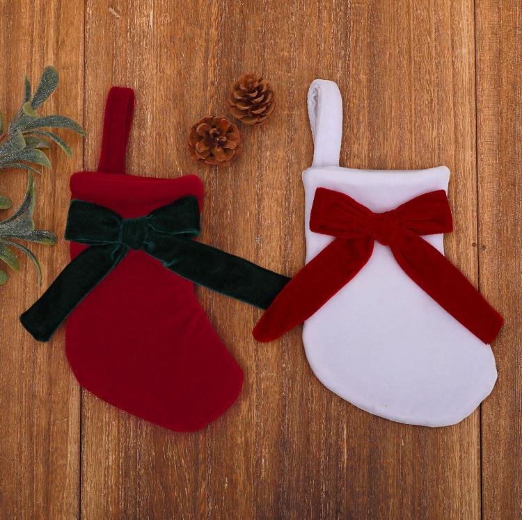 Two hanging stocking ornaments on wood: red with green bow, white with red bow