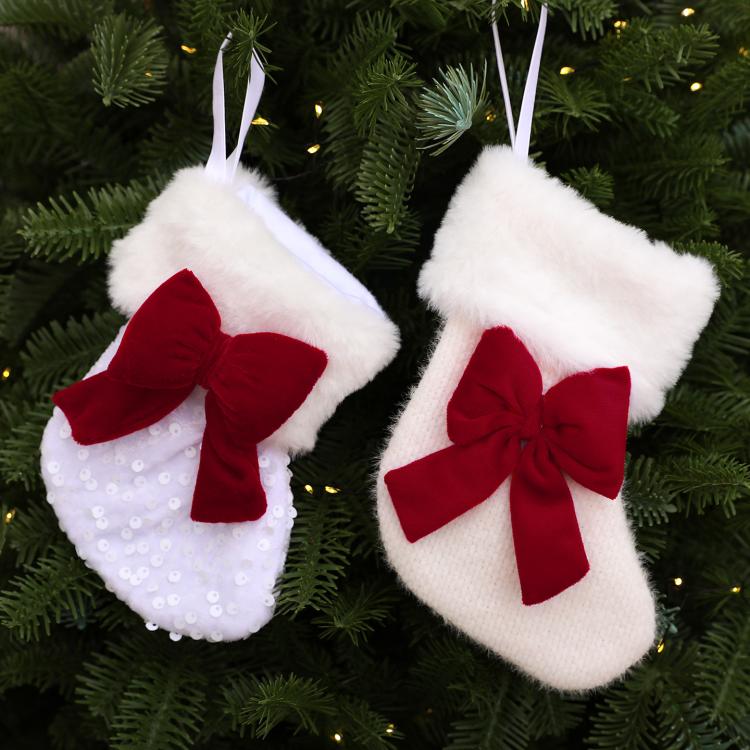 Set of two white fluffy stockings on a tree, each with a red bow