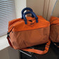 Lightweight duffel bag in orange with blue handles and adjustable shoulder strap