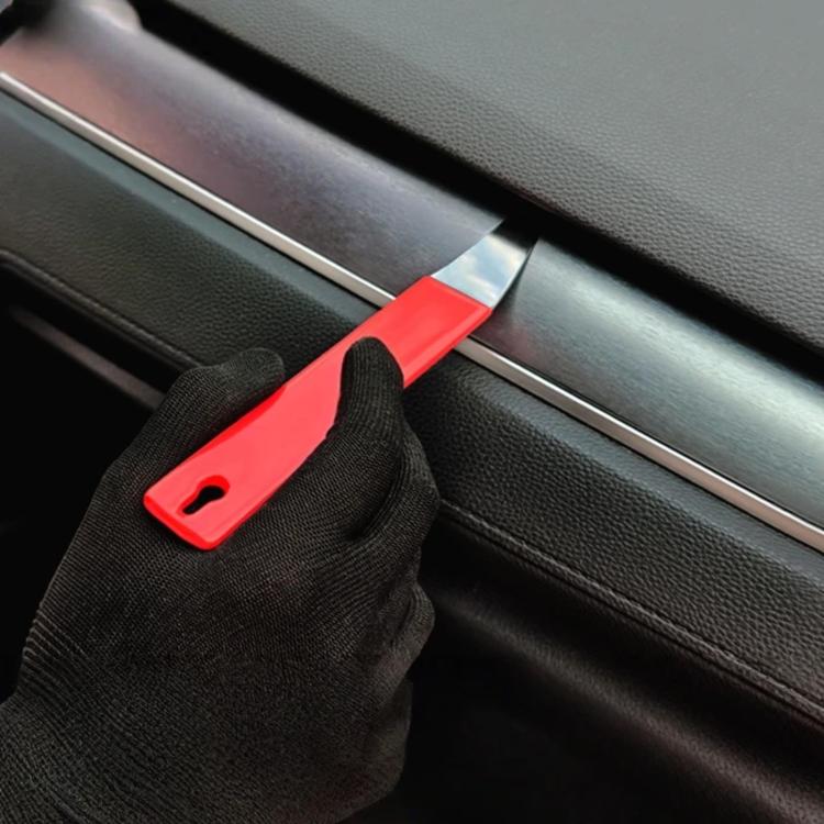 Red automotive pry bar tool used along car door seam next to gloved hand.