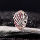 Pink glitter glass bead charm with silver skeleton hand; side view on gray surface