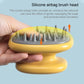 Yellow silicone scalp massage brush head with gray bristles, held for scalp massage