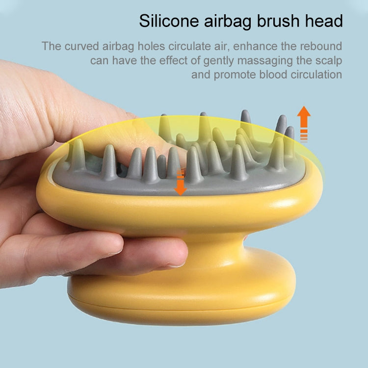 Yellow silicone scalp massage brush head with gray bristles, held for scalp massage
