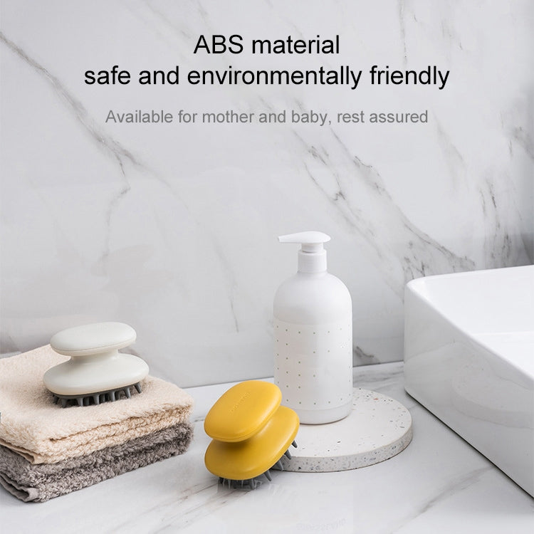 Yellow silicone scalp massage brush on countertop with marble-style tiles