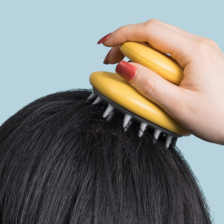 Yellow silicone shampoo brush with gray bristles being used on dark hair