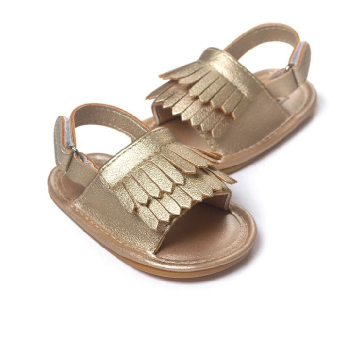Gold-toned fringed baby sandals shown from the side with open toe