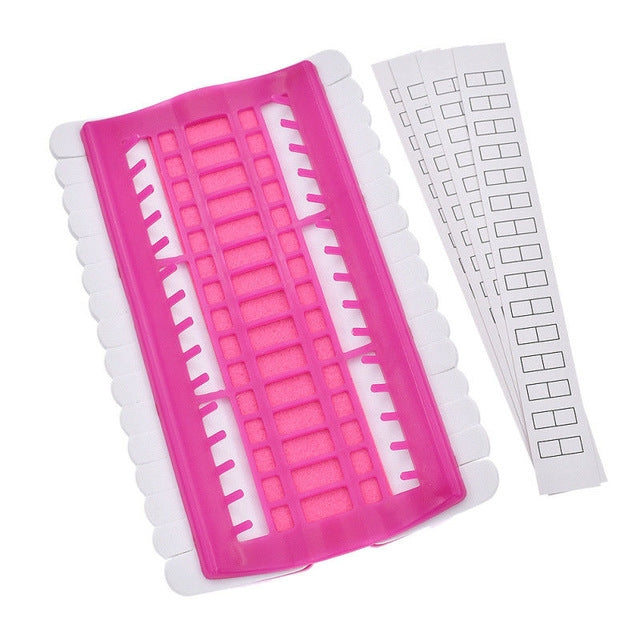 Pink cross-stitch thread organizer tool with slotted grid and two white template strips