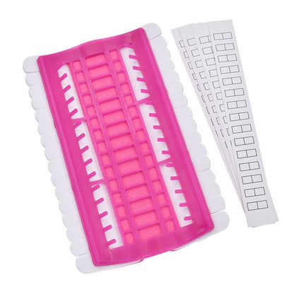 Pink cross-stitch thread organizer tool with slotted grid and two white template strips