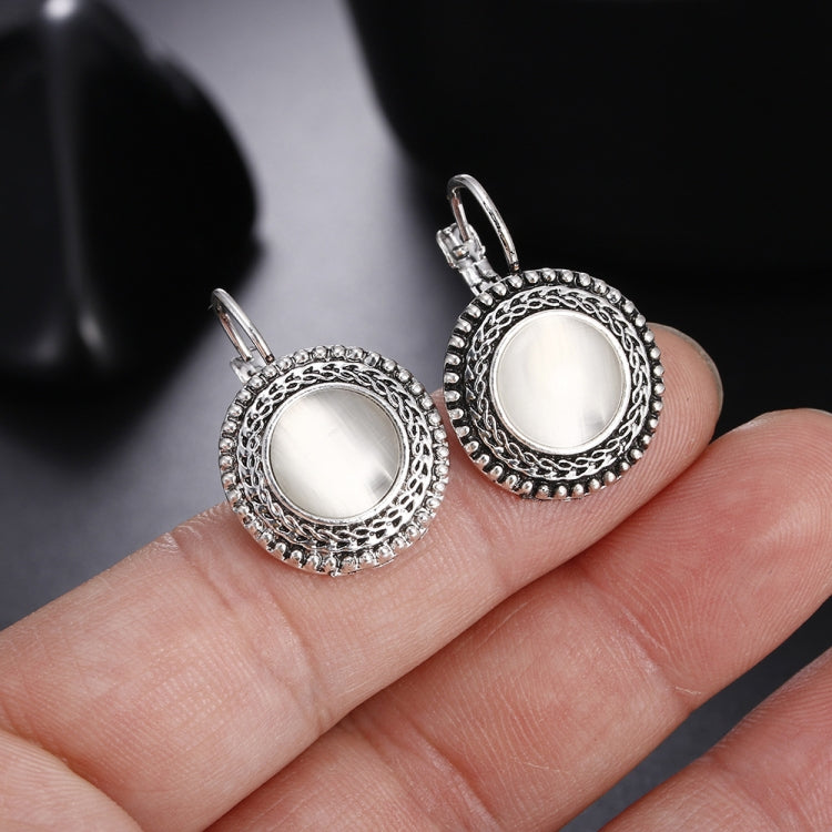 Close-up of round drop earrings with white cabochon and ornate silver filigree borders