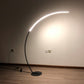Arc floor lamp glowing bright with curved light bar and black round base