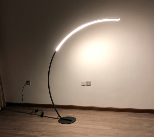 Arc floor lamp glowing bright with curved light bar and black round base