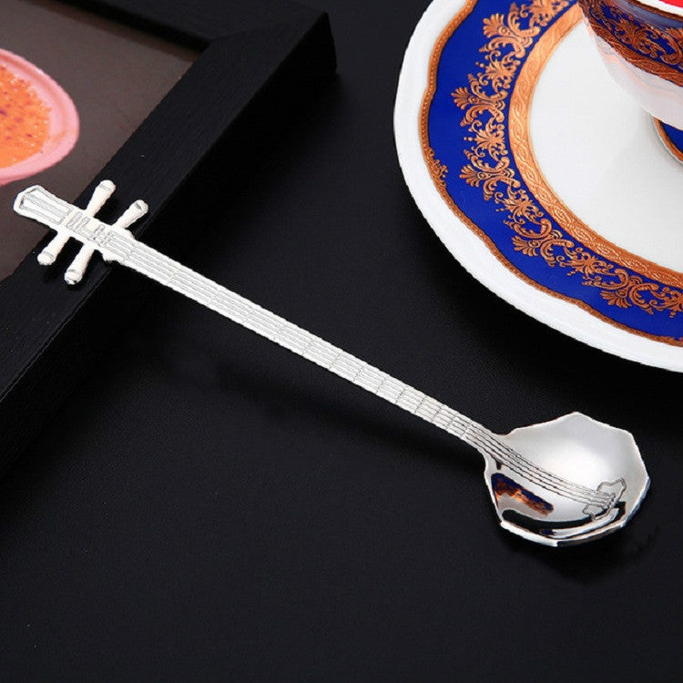 Silver guitar-shaped coffee mixing spoon beside a decorative cup