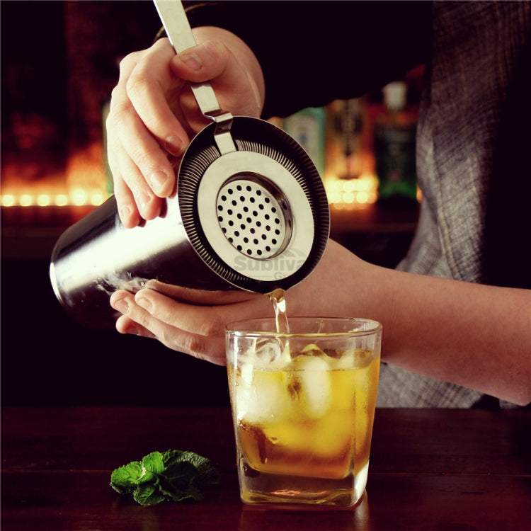 Hand holding stainless steel ice trap strainer over an iced drink, long handle