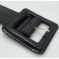 Close-up of square black glossy buckle on wide belt with gold-tone bar