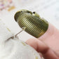 Metal sewing thimble with perforated surface and needle guide on fingertip