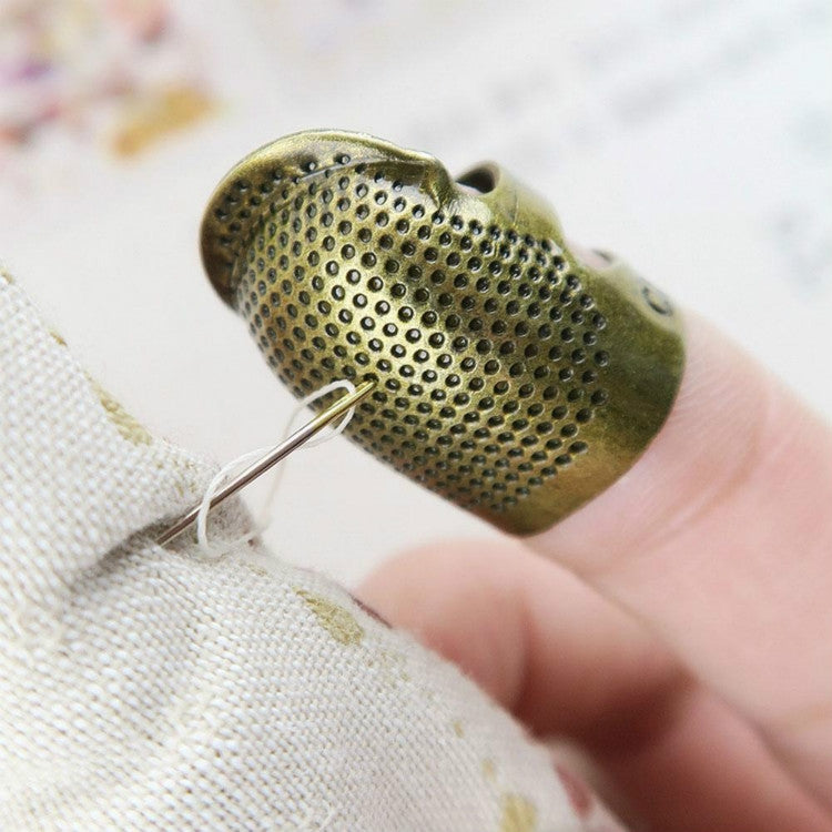 Metal sewing thimble with perforated surface and needle guide on fingertip