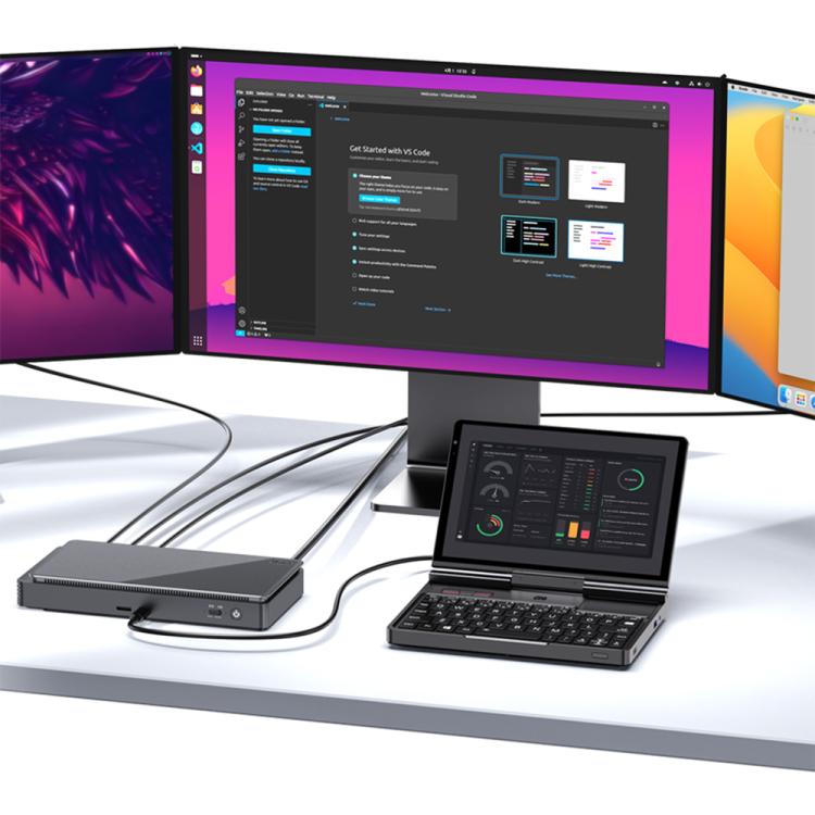 Handheld gaming PC with keyboard controls on desk beside monitors, black
