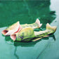 Fish-shaped green sandals floating on water, slip-on with open toe and scale texture.