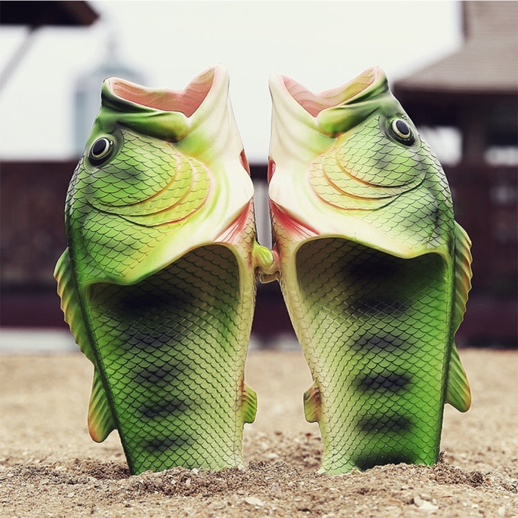 Two fish-shaped sandals in green sitting on sand, open toe slip-on design