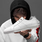Men's white low-top lace-up sneakers shown on hand, leather-look upper and rubber sole