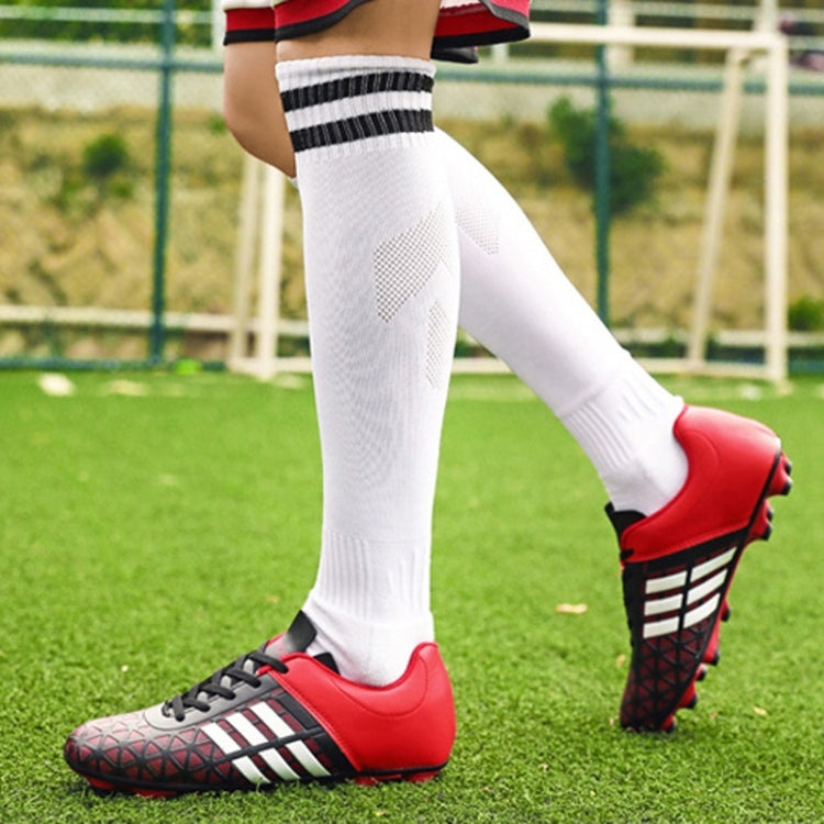 Red and black soccer cleats worn with white socks on a grass field