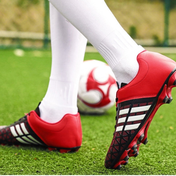 Red soccer cleats on feet with black studded sole and white socks on grass
