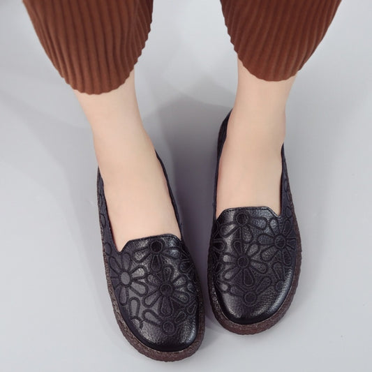 Black women's slip-on shoes with floral embroidery and brown soles, worn on feet.